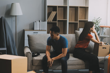 Family couple ignoring each other after a quarrel. Two people turn away and don't talk to each other. Angry young man and woman sitting back to back, with arms crossed on the sofa in the living roomの写真素材