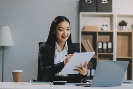 Happy young Asian businesswoman working on laptop and taking notes In office.の写真素材