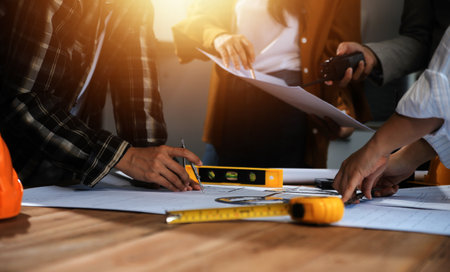 Team of multiethnic architects working on construction plans in meeting room. Engineers discussing on project in office. Mature businessman and woman standing around table working on blueprint.の写真素材