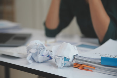 Asian women sitting in a home office With stress and eye strain.Tired businesswoman holding eyeglasses and massaging nose bridge. There are tablets, laptops, and coffee.の写真素材