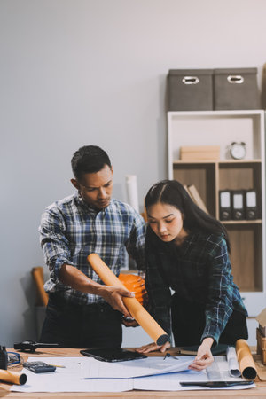 Asian young female architect discussing with japanese male building manager contractor for quality control site inspection and at house construction site in room under renovation project.の写真素材