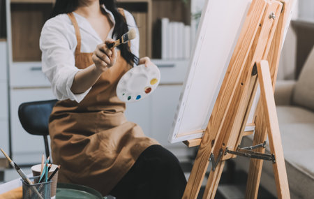 Pretty talented female painter painting on easel, making colorful sketches, creating marine landscape. Beautiful female artist painting with watercolor paints. Creativity and imagination conceptの写真素材
