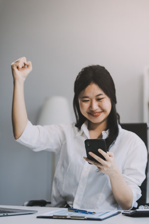 Young happy lucky woman student feeling excited winner holding cellphone using mobile phone winning online, receiving great news or sms offer on smartphone, getting new job celebrating success.の写真素材