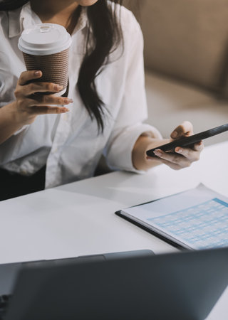 Happy Asian businesswoman working and checking work with laptop computer while having a comfortable cup of coffee at office.の写真素材