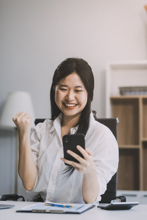Young happy lucky woman student feeling excited winner holding cellphone using mobile phone winning online, receiving great news or sms offer on smartphone, getting new job celebrating success.の写真素材