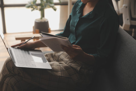 Distracted from work worried young woman sitting on couch with laptop, thinking of problems. Pensive unmotivated lady looking at window, feeling lack of energy, doing remote freelance tasks at home.の写真素材