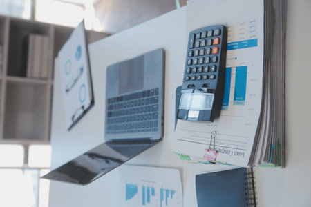 Close up view of simple workspace with laptop, notebooks, coffee cup and tree pot on white table with blurred office room backgroundの写真素材