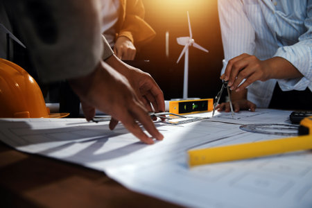 Team of multiethnic architects working on construction plans in meeting room. Engineers discussing on project in office. Mature businessman and woman standing around table working on blueprint.の写真素材