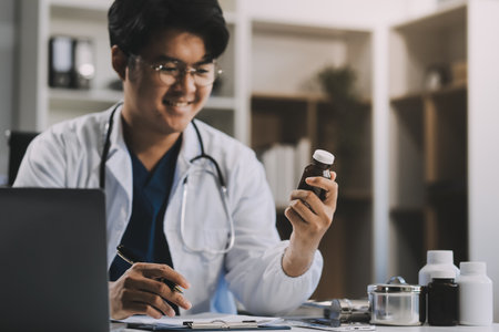 Handsome young doctor with a beard and a lab coat taking of his glasses to read an email in his laptopの写真素材