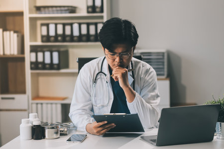 Handsome young doctor with a beard and a lab coat taking of his glasses to read an email in his laptopの写真素材