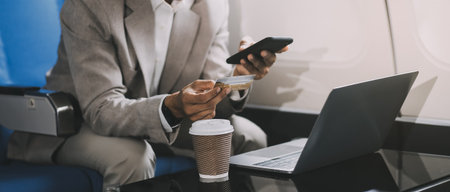 Businessman holding credit card and looking at camera near laptop in private jet