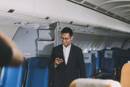 Handsome Asian male passenger takes his carry-on luggage out of the overhead locker after landing at his destination. transportation conceptの写真素材