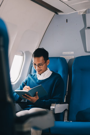 Handsome young Asian businessman or male executive manager reading a book during the flight for his business trip. Airplane or private jet conceptの写真素材