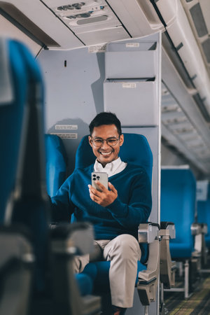 Man with dark hair is reading text message on mobile phone and speaking by phone during flying in...