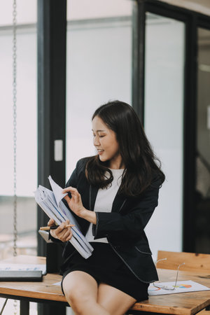 Asian businesswoman talking on phone, using laptop, looking at screen, entrepreneur manager consulting client by call, looking at computer screen, discussing project, reading informationの写真素材