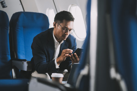Attractive Asian male passenger of airplane sitting in comfortable seat while working laptop and tablet with mock up area using wireless connection. Travel in style, work with grace.の写真素材