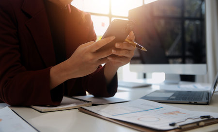 Asian businesswoman in formal suit in office happy and cheerful during using smartphone and workingの写真素材