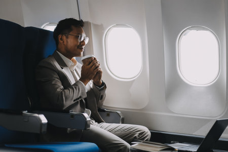 Asian businessman enjoying enjoys a coffee comfortable flight while sitting in the airplane cabin, Passengers near the window.の写真素材