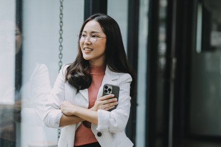 Portrait of a happy Asian businesswoman using mobile phone indoor, Asian businesswoman working in modern office.の写真素材