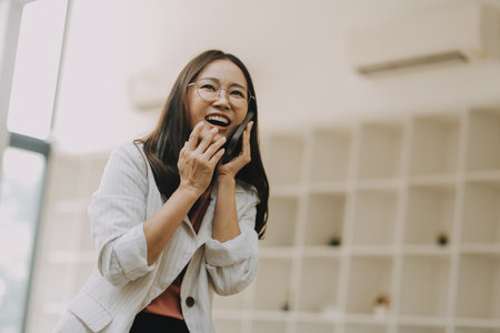 Portrait of a happy Asian businesswoman using mobile phone indoor, Asian businesswoman working in modern office.の写真素材