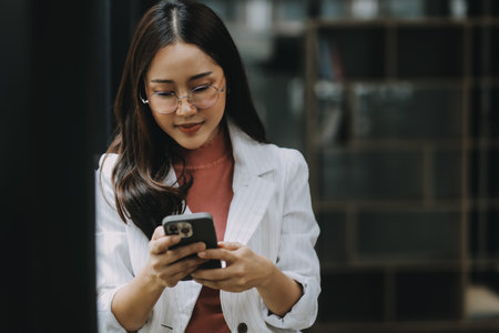 Portrait of a happy Asian businesswoman using mobile phone indoor, Asian businesswoman working in modern office.の写真素材
