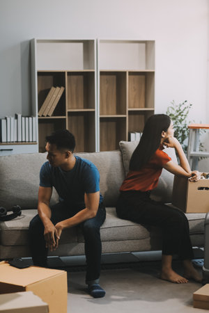 Family couple ignoring each other after a quarrel. Two people turn away and don't talk to each other. Angry young man and woman sitting back to back, with arms crossed on the sofa in the living roomの写真素材