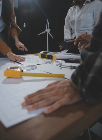 Team of multiethnic architects working on construction plans in meeting room. Engineers discussing on project in office. Mature businessman and woman standing around table working on blueprint.の写真素材