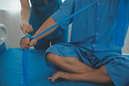 Close up hand patient doing stretching exercise with a flexible exercise band and a physical therapist hand to help in clinic room.の写真素材