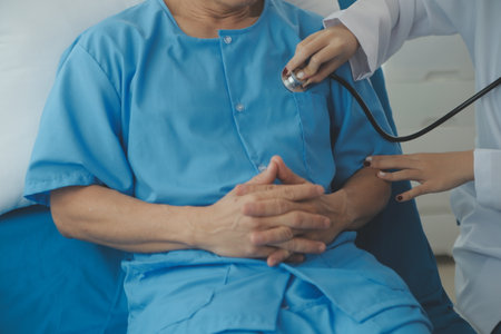 Doctor using stethoscope to listen senior man heart during examination in hospital room and wearing visor as safety precaution against coronavirus. Medical control for infections, disease.の写真素材