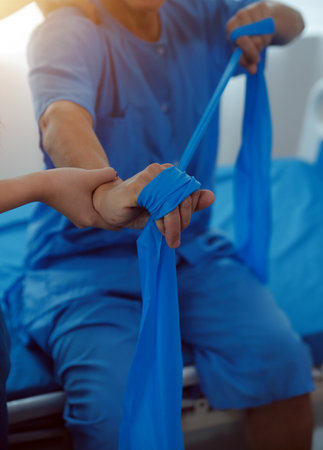 Close up hand patient doing stretching exercise with a flexible exercise band and a physical therapist hand to help in clinic room.の写真素材