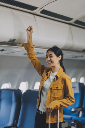 Young Female Tourist with Luggage Walking Through Airplane Cabin Ready for Travel Adventureの写真素材