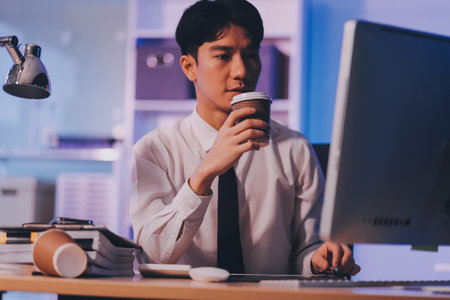 Young pensive asian man working late concentrated and serious in front of computer at night in dark office, Late night working or studying concept.の写真素材