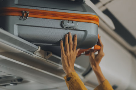Young Female Tourist Storing Luggage in Overhead Compartment on Airplane During Travelの写真素材