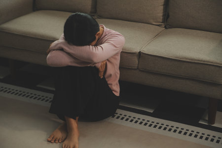 Depressed woman sitting alone on the bed with hands on head feel stress, sad and worried in the dark bedroom and low light environmentの写真素材