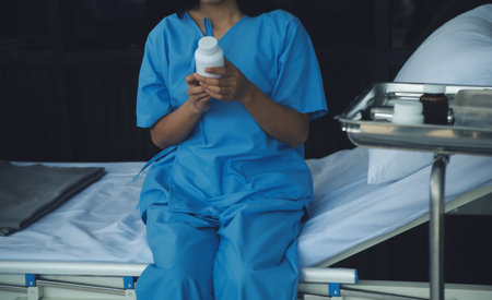 young woman sitting on the bed and looking outside window in hospital worry about her illness.の写真素材