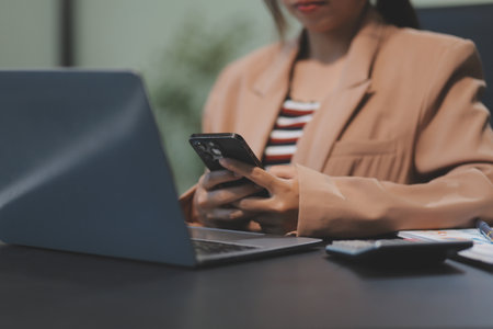 Young beautiful Asian businesswoman holding smartphone while working in the office room.