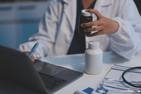 Doctor holding medicine bottle and taking notes in office.の写真素材