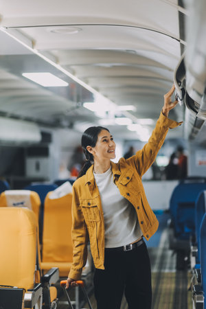 Young Female Tourist with Luggage Walking Through Airplane Cabin Ready for Travel Adventureの写真素材
