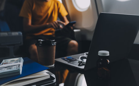 Attractive Asian businesswoman traveling on airplane playing with mobile phone while sitting in...