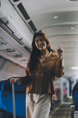 Asian woman walking with luggage in airplane cabin. Concept of travel, transportation, and journeyの写真素材