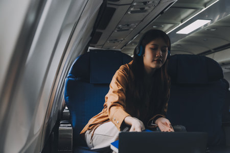 A young Asian woman, seated as an airplane passenger, contemplates dollar bills, reflecting on lucrative opportunities and aspirations towards billionaire status.の写真素材