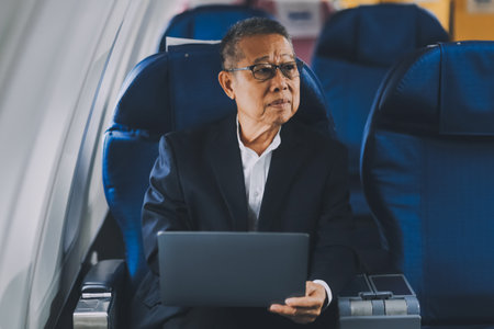 Attractive Asian male passenger of airplane sitting in comfortable seat while working laptop and tablet with mock up area using wireless connection. Travel in style, work with grace.の写真素材