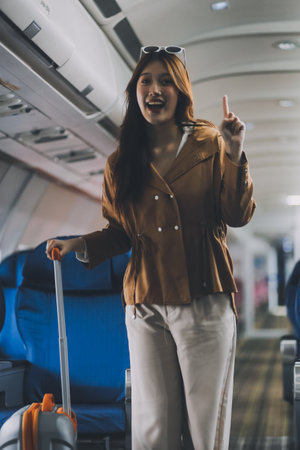 Asian woman walking with luggage in airplane cabin. Concept of travel, transportation, and journeyの写真素材