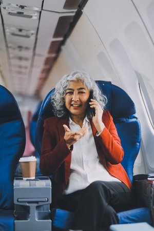 Portrait of a successful Asian businesswoman or entrepreneur in a formal suit on an airplane sitting in business class using a phone, computer laptop. Travel in style, work with grace.の写真素材