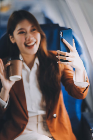 Asian woman looking at phone while sitting on airplane Technology female travelers using mobile...