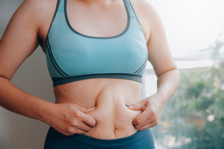 fat woman, fat belly, chubby, obese woman hand holding excessive belly fat with measure tape, woman diet lifestyle conceptの写真素材