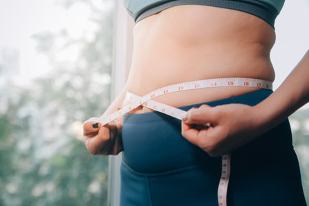 fat woman, fat belly, chubby, obese woman hand holding excessive belly fat with measure tape, woman diet lifestyle conceptの写真素材