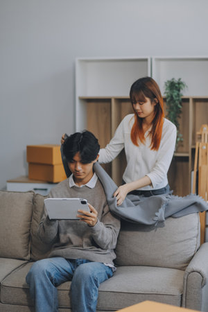Happy asian young attractive couple man and woman sit on couch use tablet shopping online furniture...