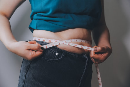 fat woman, fat belly, chubby, obese woman hand holding excessive belly fat with measure tape, woman diet lifestyle conceptの写真素材