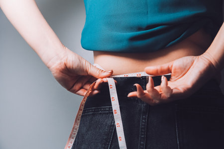 fat woman, fat belly, chubby, obese woman hand holding excessive belly fat with measure tape, woman diet lifestyle conceptの写真素材